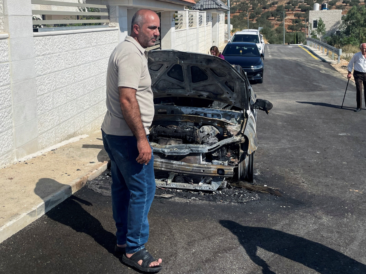 A Palestinian stands next to a damaged car following another Israeli settlers' attack in the West Bank. Photo: Reuters