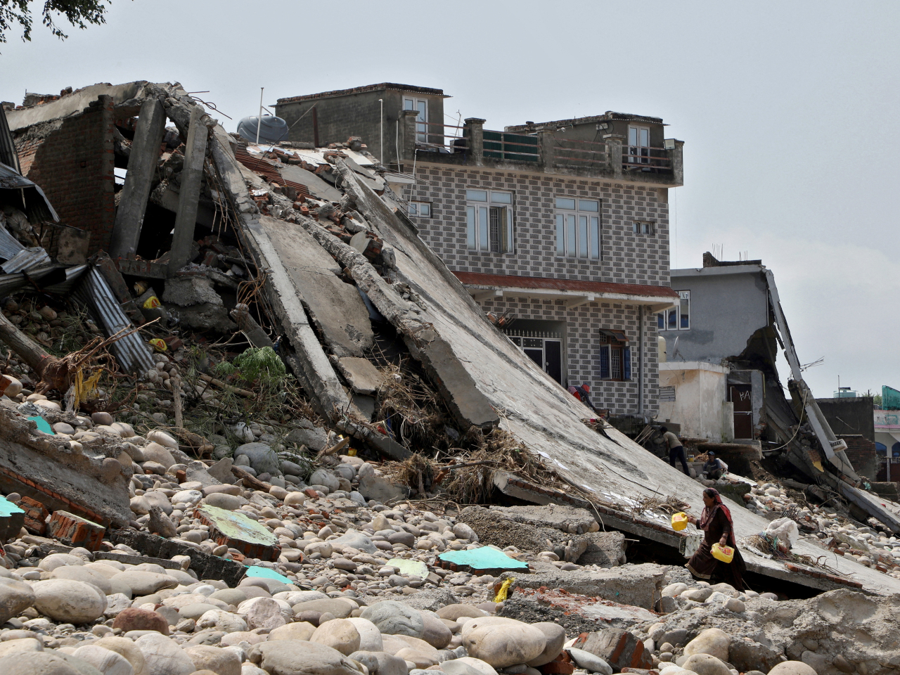 A woman carries plastic cans she found among debris of her flood-damaged house on the banks of Tawi river following heavy rain in Jammu. Photo: Reuters