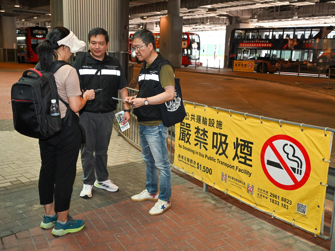 控煙酒辦人員於西九龍高鐵站附近的巴士站向旅客派發有關控煙措施的宣傳單張。（政府新聞處）