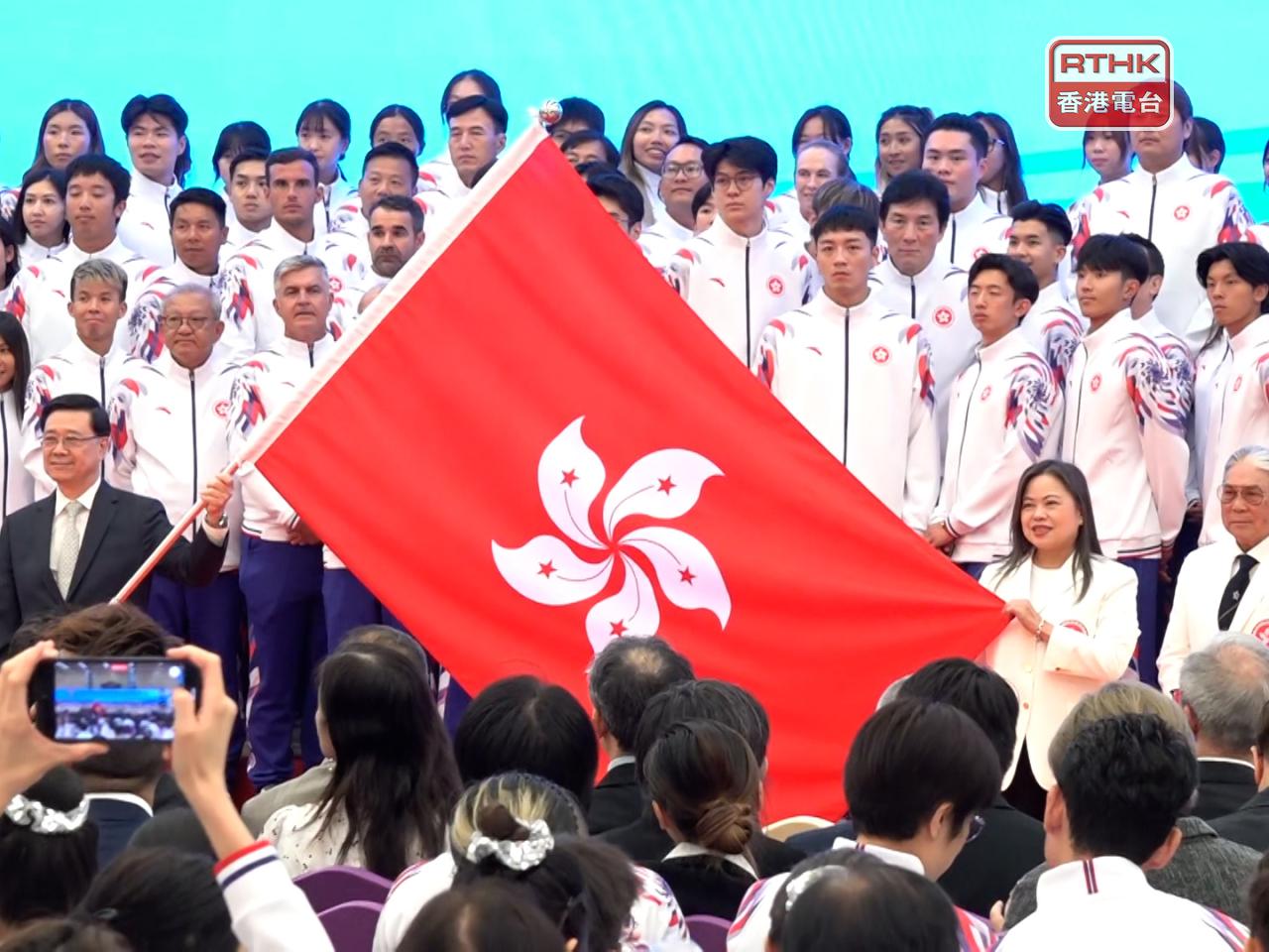 李家超（左二持旗桿）向香港特別行政區代表團授旗。（施華駿攝）