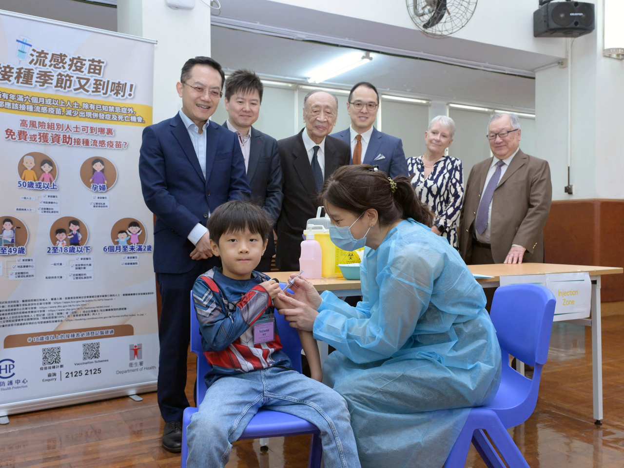 林文健(後排左一)及徐樂堅(後排左二)在學校代表陪同下視察學生接種注射式滅活流感疫苗。(政府新聞處)