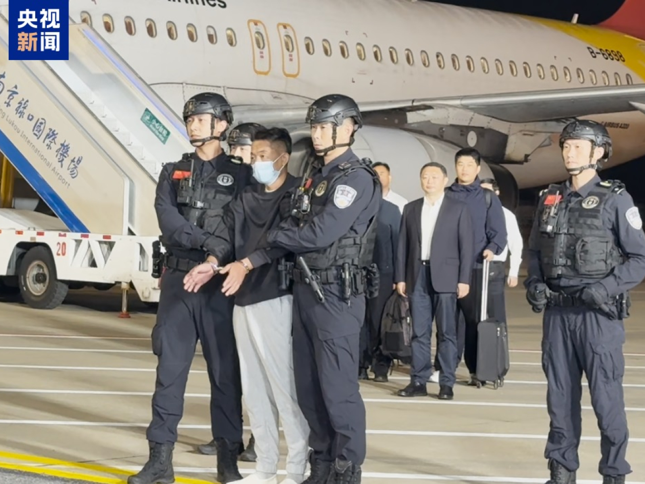 佘智江雙手鎖上手扣，由警員押解落機。（央視圖片）