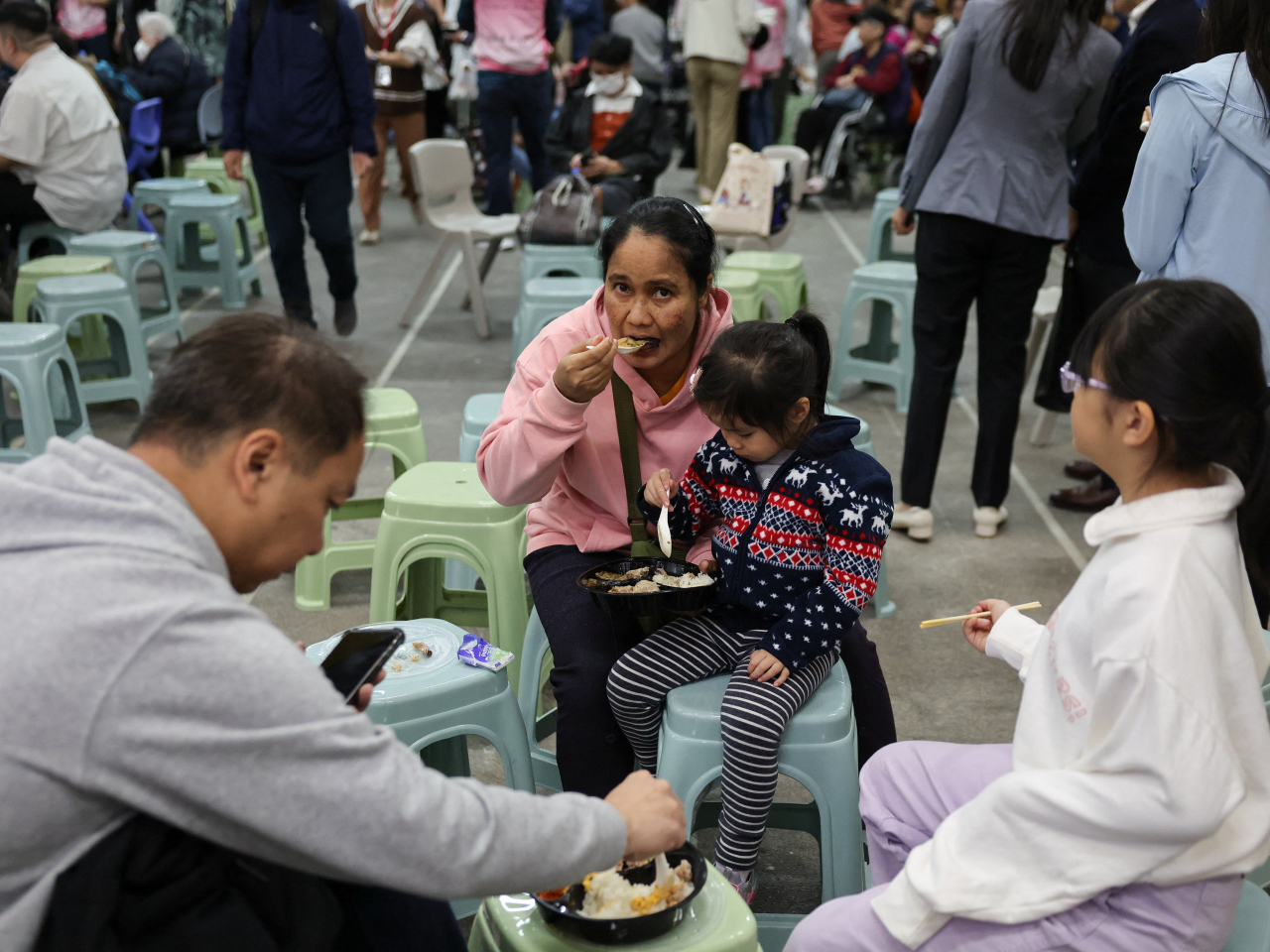 A family evacuated from one of the Wang Fuk Court buildings has a meal at one of the temporary shelters set up as the Tai Po fire rages on Wednesday. Photo: Reuters