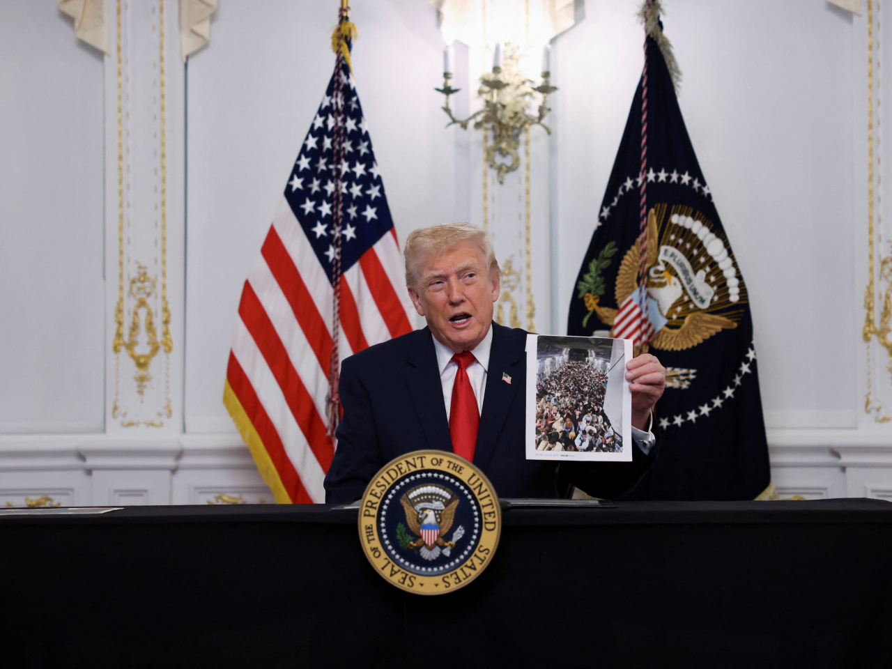 Donald Trump holds up a photo showing a US-bound plane bearing Afghans who aided Americans during the occupation, putting them at risk of Taliban retaliation. Photo: Reuters
