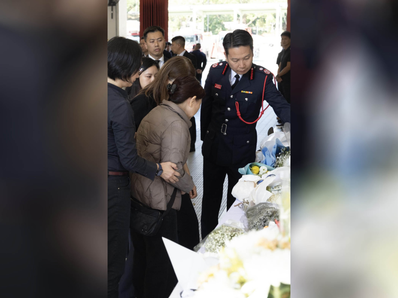 消防處助理處長鄧榮華（右一）與何偉豪家屬觀看市民致送的鮮花和心意卡。（政府新聞處）