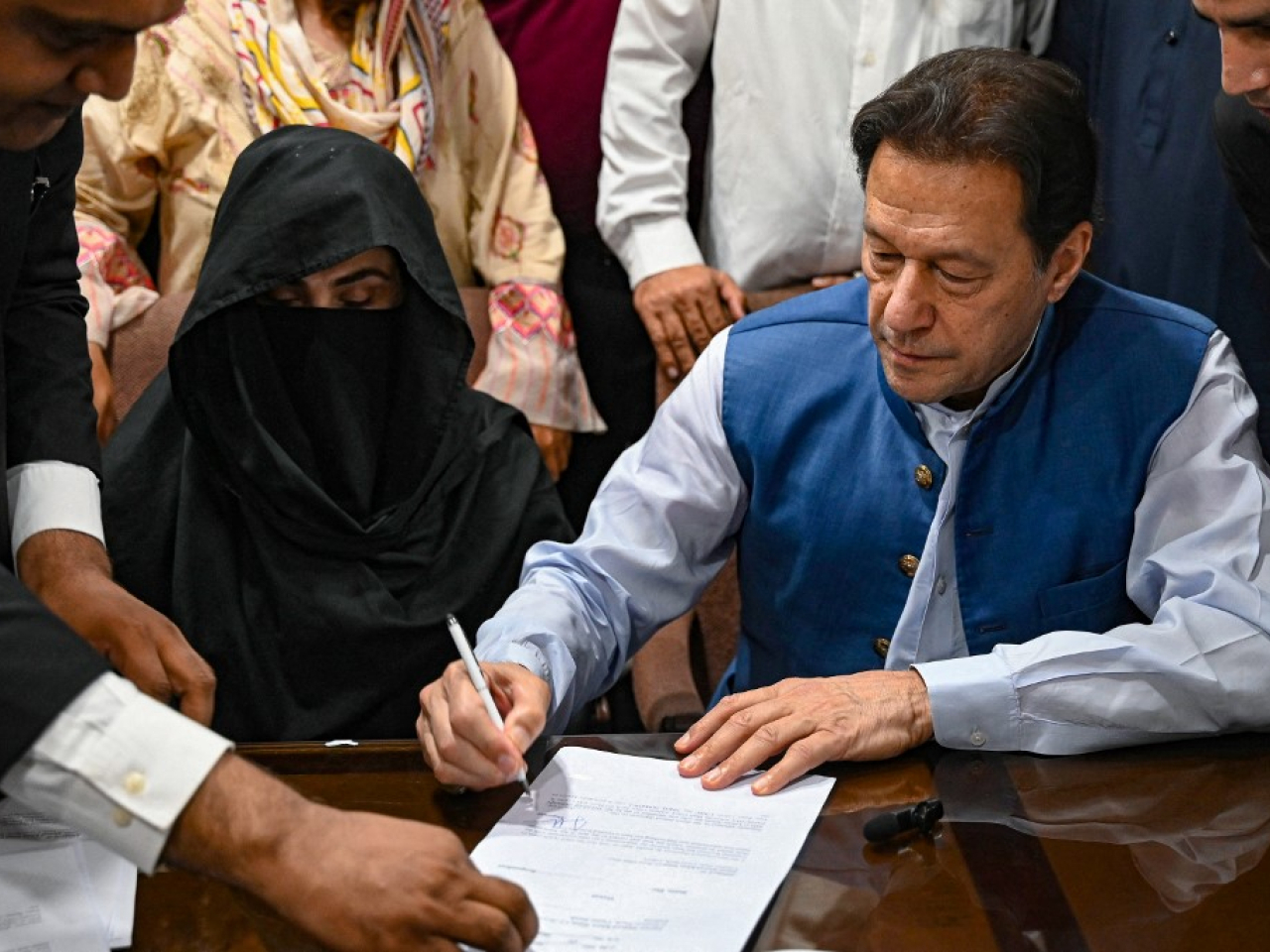 Imran Khan signs surety bonds for bail in various court cases in 2023 as wife Bushra Bibi looks on. File photo: AFP