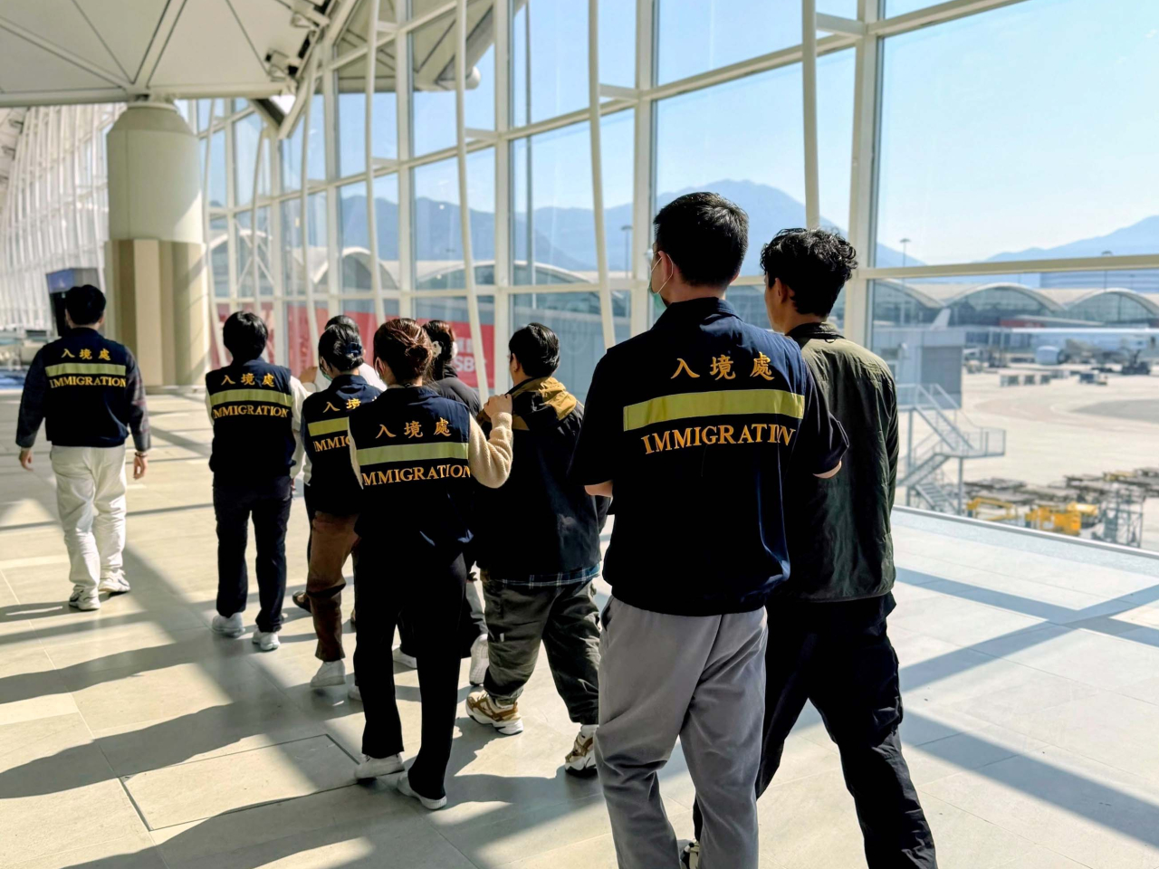 被遣返人士在入境處人員押送下離港。（政府新聞處）