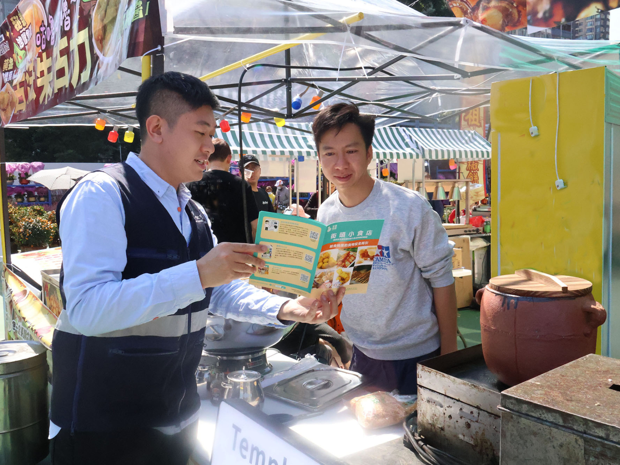 食安中心人員向快餐攤位負責人派發小冊子，提醒檔主注意食物安全。（政府新聞處）