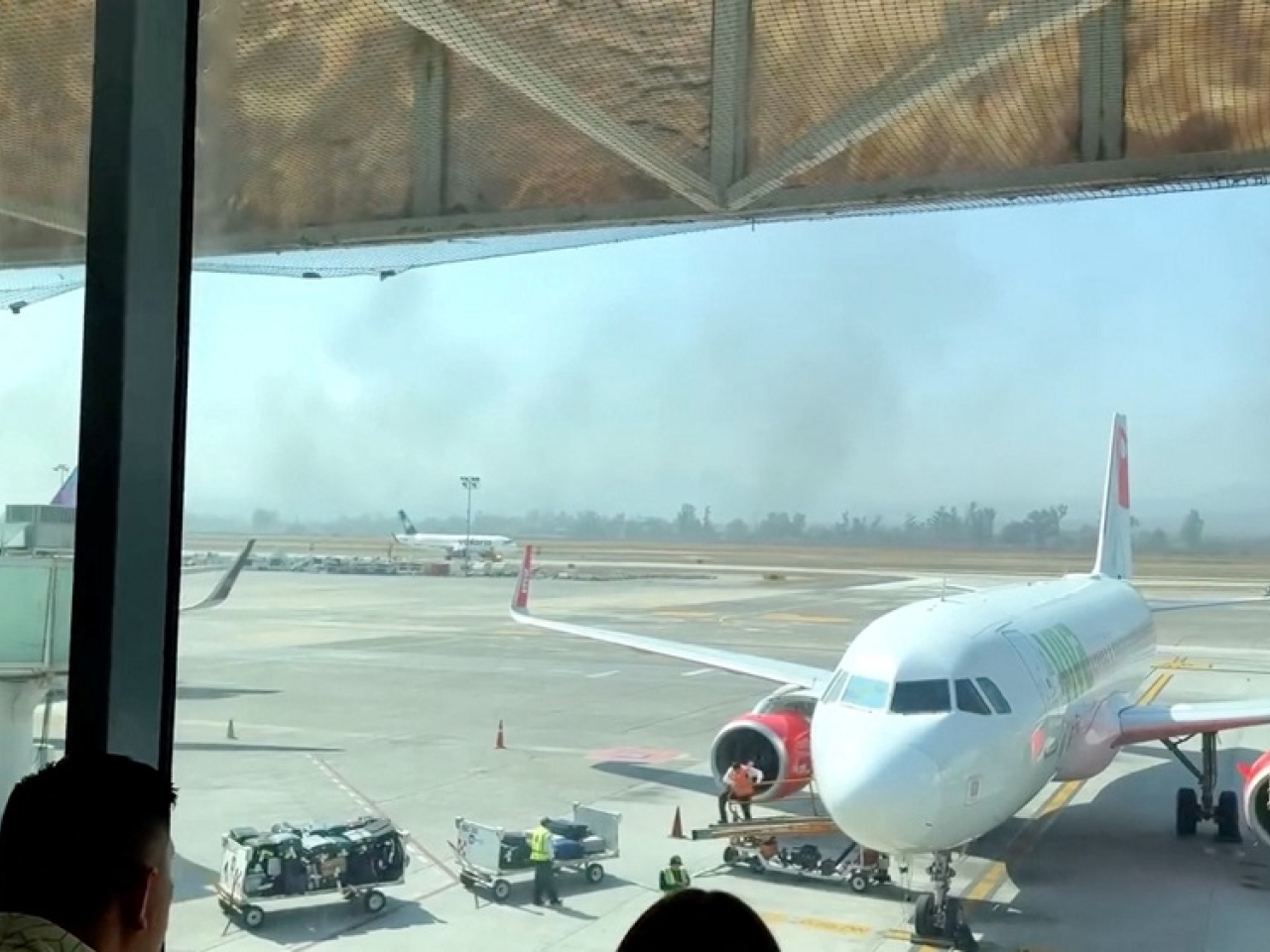 Stranded travellers watch from Guadalajara International Airport as smoke from the violence billows in the distance. Photo: Reuters