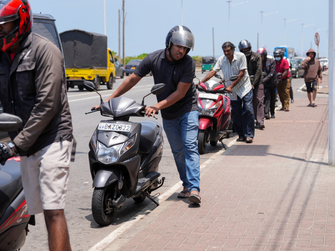 Motorcyclists go with their feet when push comes to shove while lining up at a petrol station in Colombo, Sri Lanka. File photo: Reuters