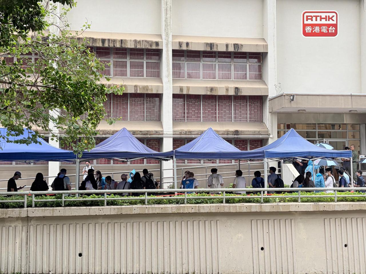 不少居民冒雨到社區會堂外輪候登記，當局設置大型帳篷為居民擋雨。（鄧鈞尤攝）