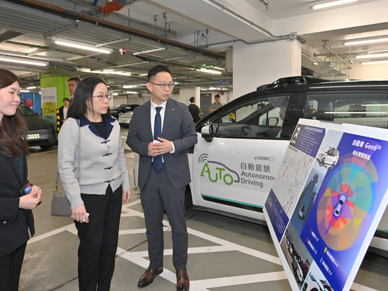 運輸署表示，本港的自動駕駛車輛測試一直大致暢順，顯示香港在推動自動駕駛的穩健發展，與海內外各地水平相若。圖示運輸署署長謝詠誼（中）視察其中一個於機場島進行的測試項目，並聽取先導營辦人介紹項目進展。（政府新聞處提供）