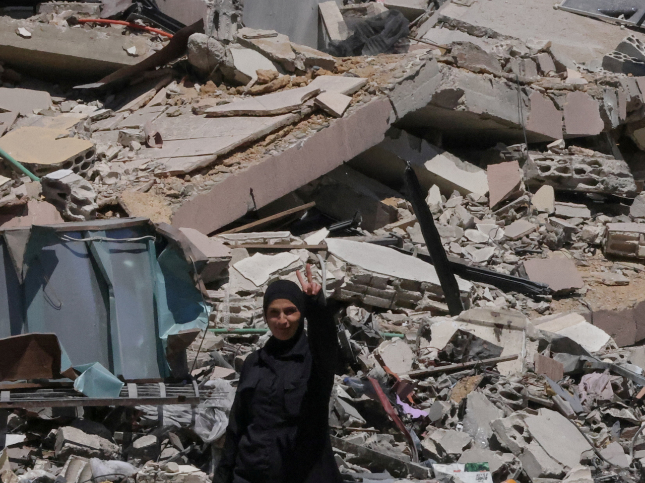 A woman returning to her village after displacement by the war flares a victory sign near her neighbour's house that was destroyed by an Israeli strike, in southern Lebanon. Photo: Reuters