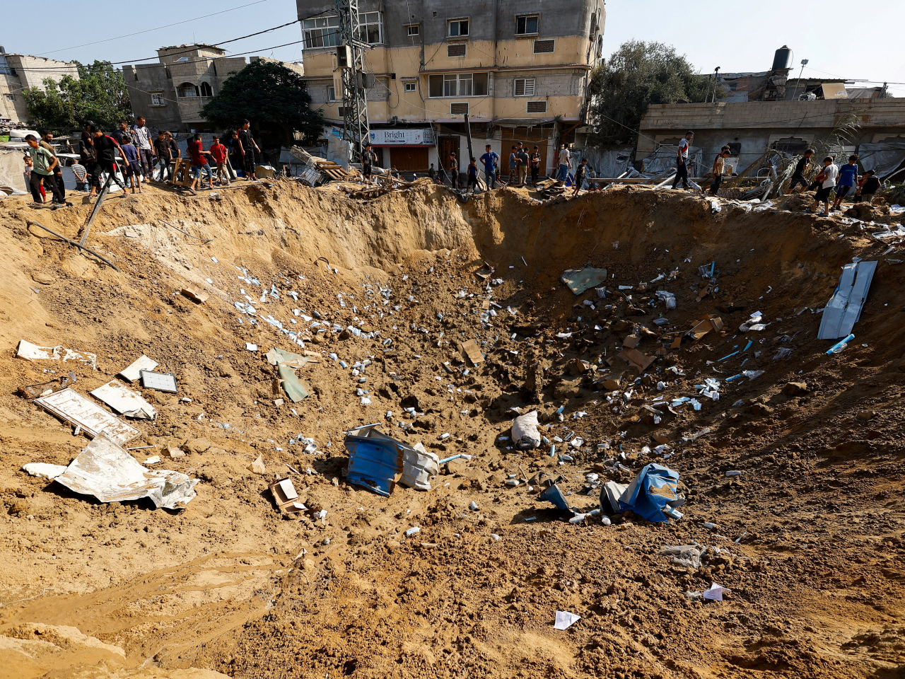 Palestinians stand by a crater, after an Israeli strike on a medicine warehouse in the central Gaza Strip. Photo: Reuters