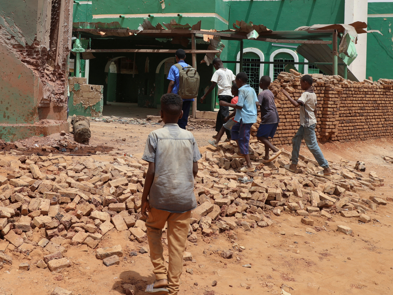 Children walk next to a collapsed mosque wall after a drone strike in Bahri city, Sudan. Photo: Reuters