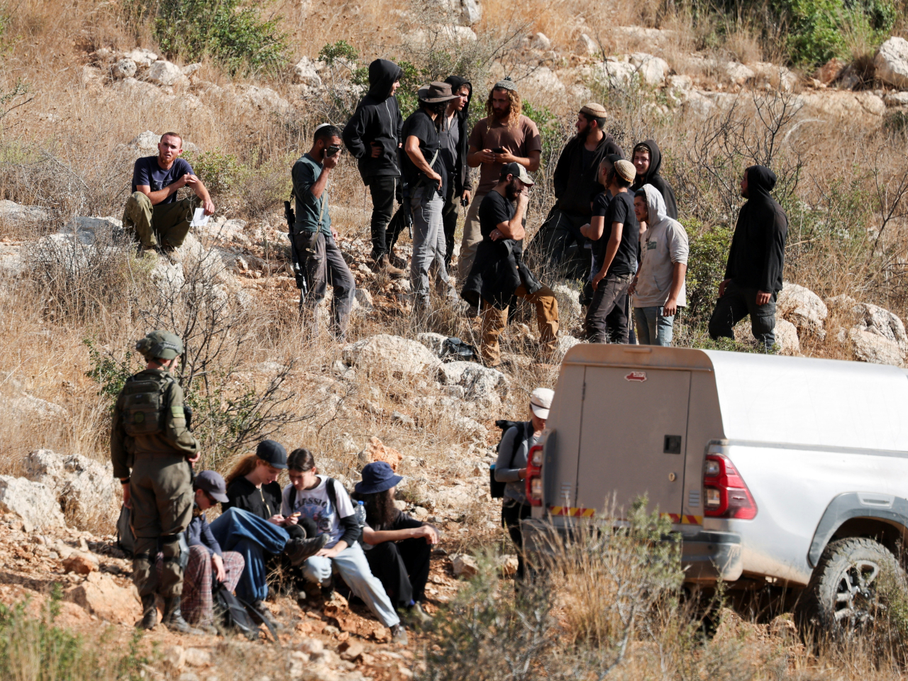 Israeli settlers sit next to soldiers as they prepare to pick olives at Palestinian-owned groves near Ramallah, West Bank. Photo: Reuters